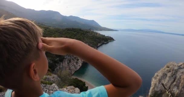Primo piano del viaggiatore ragazzo con il braccio alzato sulla cima della montagna guardando la vista del mare Adriatico e montagne rocciose con foresta verde al tramonto — Video Stock