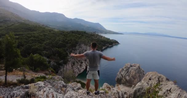 Visão traseira do caminhante masculino que atingiu o topo da montanha acima do mar Adriático na Dalmácia no fundo montanhas rochosas com floresta verde ao pôr do sol — Vídeo de Stock