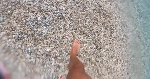 Крупним планом чоловічі ноги йдуть вперед на гальковому пляжі чистого моря . — стокове відео