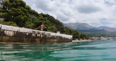 Genç çocuk yaz tatilinde Hırvatistan 'da iskeleden açık mavi denize takla atıyor.