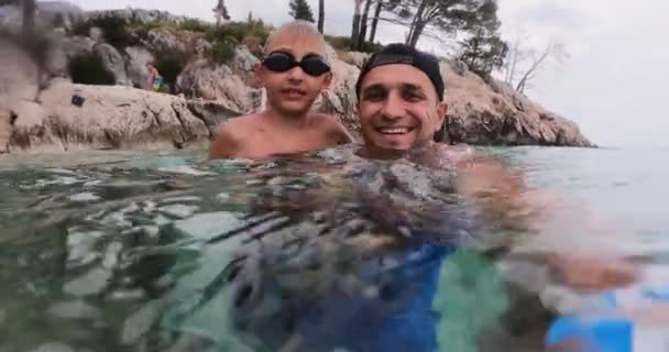 Handsome smiling man with has little son in swimming goggles enjoying summer vacation swimming in clear Adriatic sea, looking at camera. Nature, healthy lifestyle — Vídeo de stock