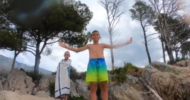 Αξιαγάπητο αγόρι που στέκεται πάνω σε βράχια με υψωμένα χέρια μετά το μπάνιο του στη θάλασσα δίπλα στην παραλία κατά τη διάρκεια των καλοκαιρινών διακοπών. Η Κροατία στη Δαλματία — Αρχείο Βίντεο