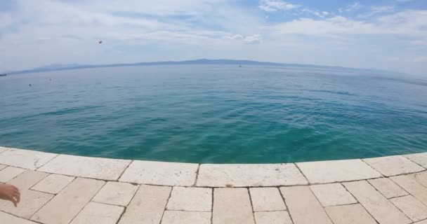 Two slender guys jumping from pier into clear sea during summer holiday on blue sky and mountains background. Back view — 비디오