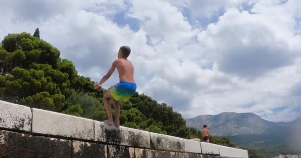 Young caucasian boy jumping somersault back from pier into clear blue sea during vacation on summer holiday in Croatia. Healthy lifestyle and happy beach vacation. — Vídeo de Stock