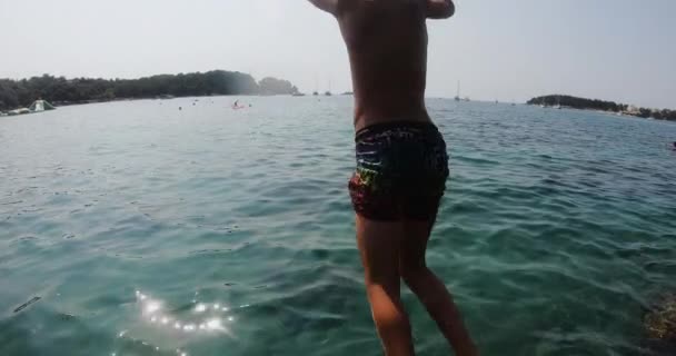 Back view of caucasian teen boy in swim shorts while diving from sea stone at clear blue sea, stones can be seen bottom of sea. Summer vacation, lifestyle concept — Stockvideo