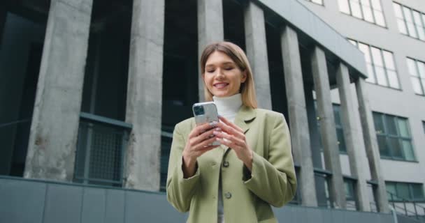 Başarılı genç iş kadını iş bölgesinde akıllı telefon kullanıyor. Beyaz kadın çalışan girişimci kentsel arka planda akıllı telefon kullanıyor — Stok video