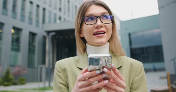 Красивая молодая кавказская деловая женщина в очках пользуется телефоном гуляет по улицам городской техники мобильной печатной связи, здания офисного фона — стоковое видео