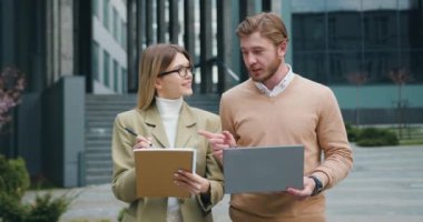 Başarılı genç erkek ve kadın öğrenciler birlikte okuyorlar, dizüstü bilgisayar kullanıyorlar, üniversite kampüsünden yürüyerek uzaklardan öğreniyorlar. Erkek ve kadın serbest çalışan teneffüste dışarıda çalışıyor.
