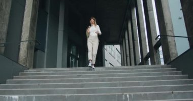 Aktif ve kendine güveni tam genç bir kadın merdivenlerden aşağı inerken harika bir yürüyüş sırasında gülümsüyor. Dışarıda.
