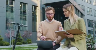 Şehir finans bölgesinde bankta oturan güzel görünümlü bir çift laptopla çalışıyor, notlar alıyor, gülümsüyor, serbest çalışan insanlar, dışarıda.