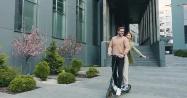 Modern ofis merkezinin yakınında birlikte elektrikli scooterla gezen mutlu beyaz bir çift. Dışarıda, yaşam tarzı konsepti