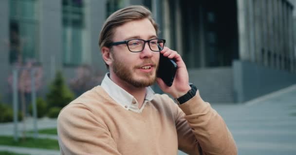 Detailní záběr úspěšného vousatého muže v brýlích mluvící mobilní telefon ve finanční čtvrti města. Venku. — Stock video