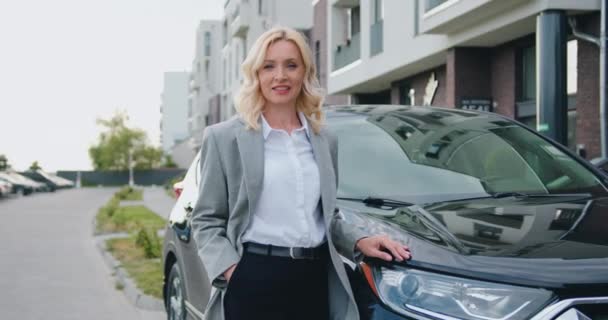 Retrato de meia-idade empresária de pé perto estacionado carro no estacionamento olhar para a câmera sorrindo. — Vídeo de Stock
