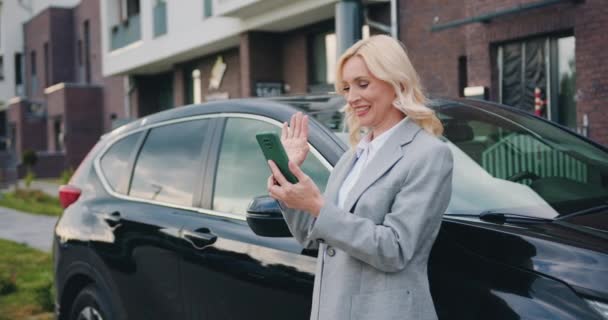 Mooie zakenvrouw in een jasje staat naast de auto en maakt een videogesprek. Conferentie met zakenpartners om nieuwe zakelijke ideeën te bespreken. — Stockvideo