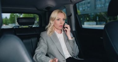 Olgun bir iş kadını taksinin arka koltuğunda oturuyor ya da akıllı telefondan konuşuyor. Modern araba kuaföründe cep telefonuyla konuşan neşeli iş kadını. Yavaş çekim.