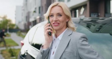 Güzel bir iş kadını cep telefonuyla konuşuyor. Evinin yakınına park etmiş siyah arabasına yaslandığında iş görüşmesine cevap veriyor. Açık havada. Yavaş çekim