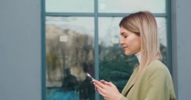 Yakın plan başarılı kadın akıllı telefonuyla sokakta yürüyor ve akıllı telefon kullanarak arkadaşlarıyla sohbet ediyor. İletişim, sosyal ağlar, online alışveriş konsepti. Yavaş çekim.