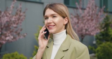 Kapatın. Modern iş kadını dışarıda dikilip cep telefonuyla konuşuyor. Konuşan portre kızı şehir sokağında akıllı telefon kullanıyor. Yavaş çekim.
