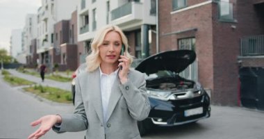 Arabasının kaputunun önünde duran resmi giysili endişeli kadın, servis merkezini arıyor, çekici ya da teknik destek bekliyor. Açık havada. Yavaş çekim