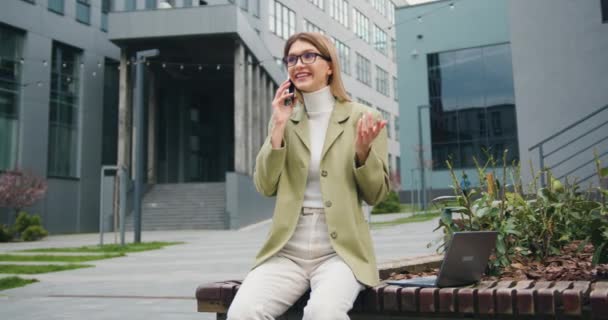 身穿夹克衫的年轻快乐的女商人正在现代办公楼外打电话 生活方式的概念 慢动作 — 图库视频影像