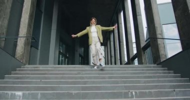Merdivenlerden inerken aktif olarak dans eden neşeli genç bir kadın. Yavaş parola.