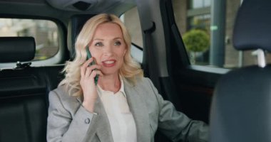 Çekici yetişkin beyaz iş kadını arabada cep telefonuyla konuşuyor. Beyaz bir kadın arabanın arka koltuğunda oturuyor ve önemli bir çağrıya cevap veriyor. Serbest çalışma konsepti. Yavaş çekim