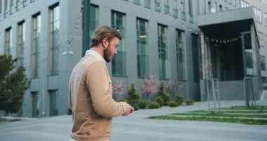 Şehir caddesinde yürürken genç ve yakışıklı iş adamının cep telefonuyla mesajlaştığı görüntüler. Yavaş çekim.