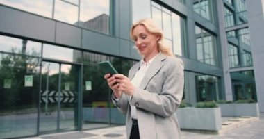 Güzel ve mutlu beyaz kadın portresi sokak şehrinde yürürken akıllı telefondan dışarıda yazarken. Şehir caddesinde boş konsept akıllı telefon. Yavaş çekim