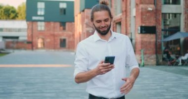 Beyaz tişörtlü çekici bir adam dışarıda telefonla konuşurken mesaj yolluyor. Neşeli sakallı adam akıllı telefonunu kullanarak iyi haberler veriyor. Yavaş çekim.