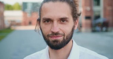 Beyaz bir delikanlının gülümseyip dışarıda kameraya baktığı yakın plan. Şehir sokağında mutlu ve yakışıklı bir genç adamın portresi. Yavaş çekim