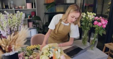 Florist woman using laptop. owner modern small flower shop working on laptop computer and cheking ordering plants, emails, and typing messages. Slow motion.