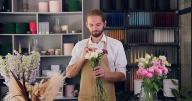 Çiçekçi dükkanının sahibi satış masasının arkasında kameraya bakıyor. Çiçekçide çalışan erkek girişimci. Yavaş çekim.