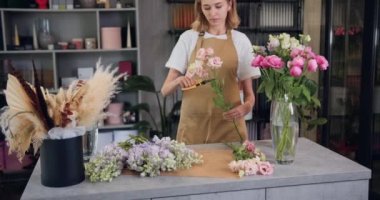 Woman florist working with fresh flowers standing in work place. Blonde girl cuts gypsophila flowers with scissors to make a bouquet.