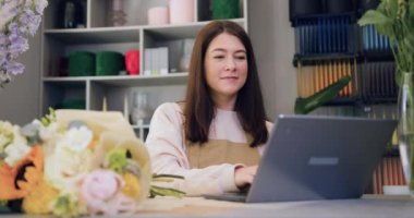 Woman flower shop worker works at a laptop. Professional florist accepts online orders from customers on website of his own store. Small business concept. Slow motion.