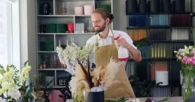 Professional florist worker watering and spraying flowers. Male seller in apron taking care of plants indoors in own flower shop. Slow motion.