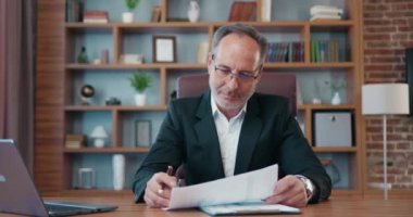 Portrait of good-looking confident experienced bearded ceo in formal wear which sitting at the table in well-designeted office room and browsing financial reports