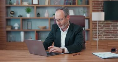 Portrait of handsome concentrated experienced successful bearded ceo or head of company in stylish business suit which sitting in front of laptop and typing in modern office