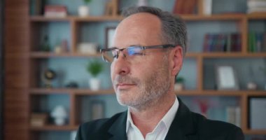 Close up portrait of likable successful high-skilled bearded head of company in eyewear dreamly looking aside in his workplace and then looking at camera