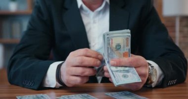 Close up of unrecognizable rich motivated bearded office manager in formal wear which sitting at his workplace in office and calculating dollars banknotes as a reward after profitable contract,part of