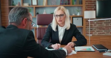 Good-looking experienced successful adult businesspeople sitting at the table in modern office and brainstorming over joint business project using financial documents and reports