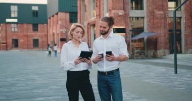 Stylish two business partner walking talking. Business couple talking about work on city walk near business center. man and woman professional discussing data on table outdoor. Slow motion.