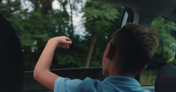 后视镜快乐的孩子从车窗伸出手来 在与家人的旅行中 男孩挥挥手向车窗外示意 慢动作 — 图库视频影像