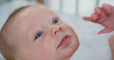 Yeni doğmuş bir bebeğin gülümseyen yüzü, parlak bir odada, yatakta yatar. Emzik kullanan yeni doğmuş bir erkek bebek. Küçük bebek yatakta yatıyor. Yavaş çekim.