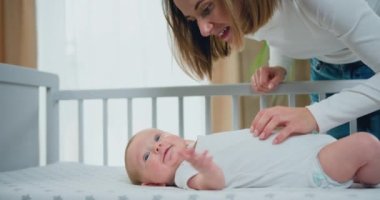 Yakından bir portre. Güzel anne beşikteki sevimli bebeği oynatıyor ve sakinleştiriyor. Gülümseyen bir anne ve küçük sevimli bir bebek. Mutlu aile kavramı. Yavaş çekim.