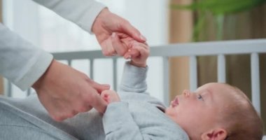 Yakın çekim. Çocuk Beşiğinde Sırtüstü Uzanıp Annelerin Elleriyle Oynarken Yeni Doğan Bebek. Anne, yeni doğmuş çocuğun elini tutuyor. Yavaş çekim.