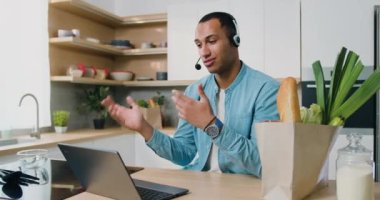 Mutfakta gülümseyen Afrikalı Amerikalı adamın portresi online toplantı yapıyor ve web kamerasına bilgisayarlı konferans görüntülerini aktarıyor. Evden çalışıyorum. Serbest çalışıyorum. Yavaş çekim.
