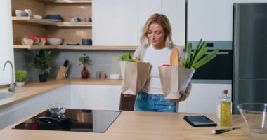 Kadın süpermarketten alışverişle dönüyor. Modern mutfakta duran kağıt eko-paketleme çantasından alışveriş yapan kadın tüketici. Yavaş çekim.