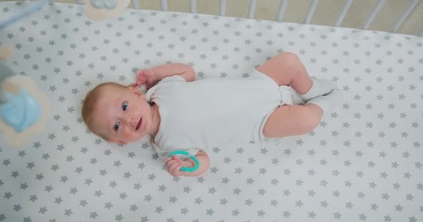 笑着躺在背上的可爱的男婴的画像 并在婴儿床上积极地移动着他的胳膊和腿 将快乐的2个月大的婴儿抱着牙齿在婴儿床里玩耍 尽收眼底 慢动作 — 图库视频影像