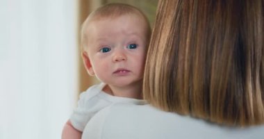 Sevgi dolu genç anne kucağında sevimli ve gülümseyen bebeğini tutuyor. Erkek bebek portresi. Kapalı alanda vurulmuş, annesinin kollarında yeni yürümeye başlayan bir çocuk. Çocukluk ve annelik kavramı. Yavaş çekim