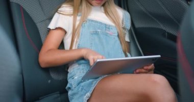 Güzel, pozitif, kaygısız, modaya uygun kıyafetleri olan 12 yaşında sarışın bir kız, kablosuz kulaklık takıyor, tablet cihazında bir şey arıyor ve otomatik otururken duygusal tepki veriyor.